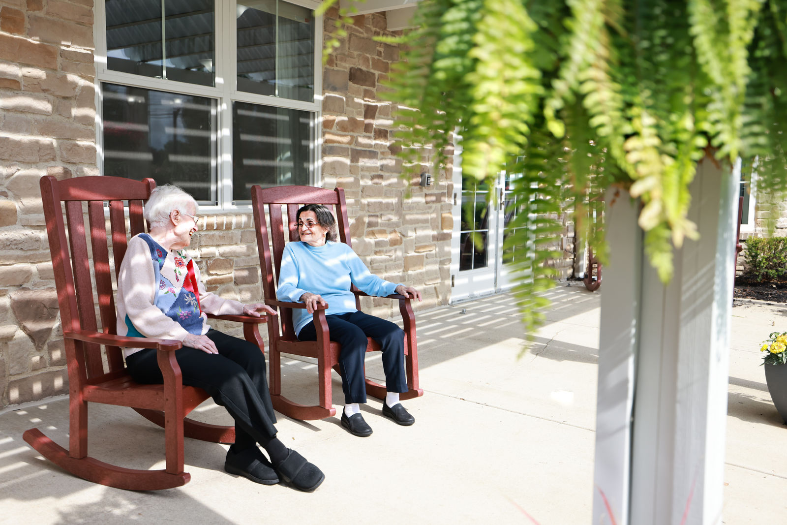 Two senior women sitting in rocking chairs on the porch of their senior living community center