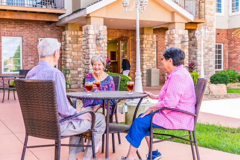 3 senior citizens who live at a senior living community sitting outside in the shade