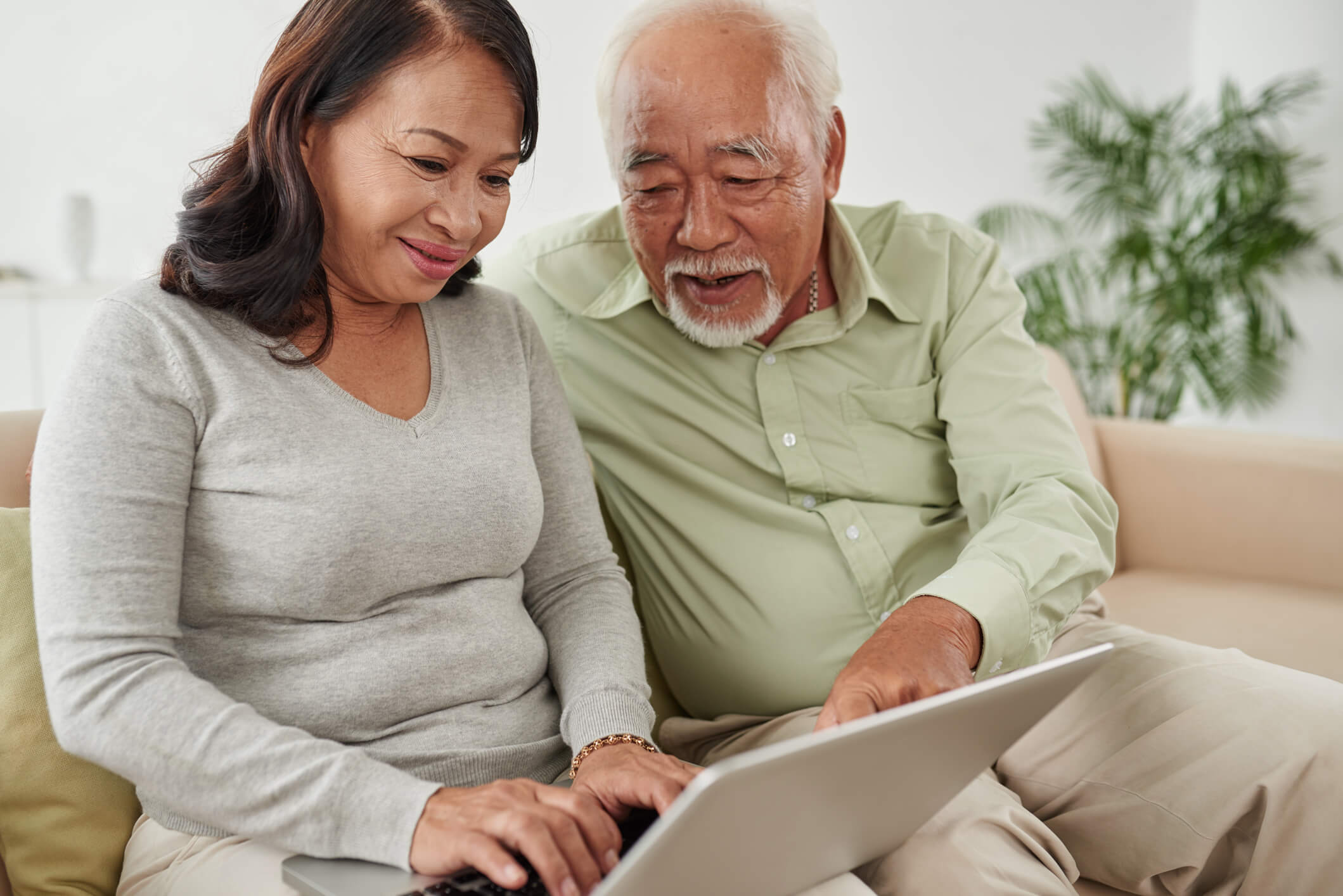 Senior couple sitting on couch using laptop to research the best senior living communities near them