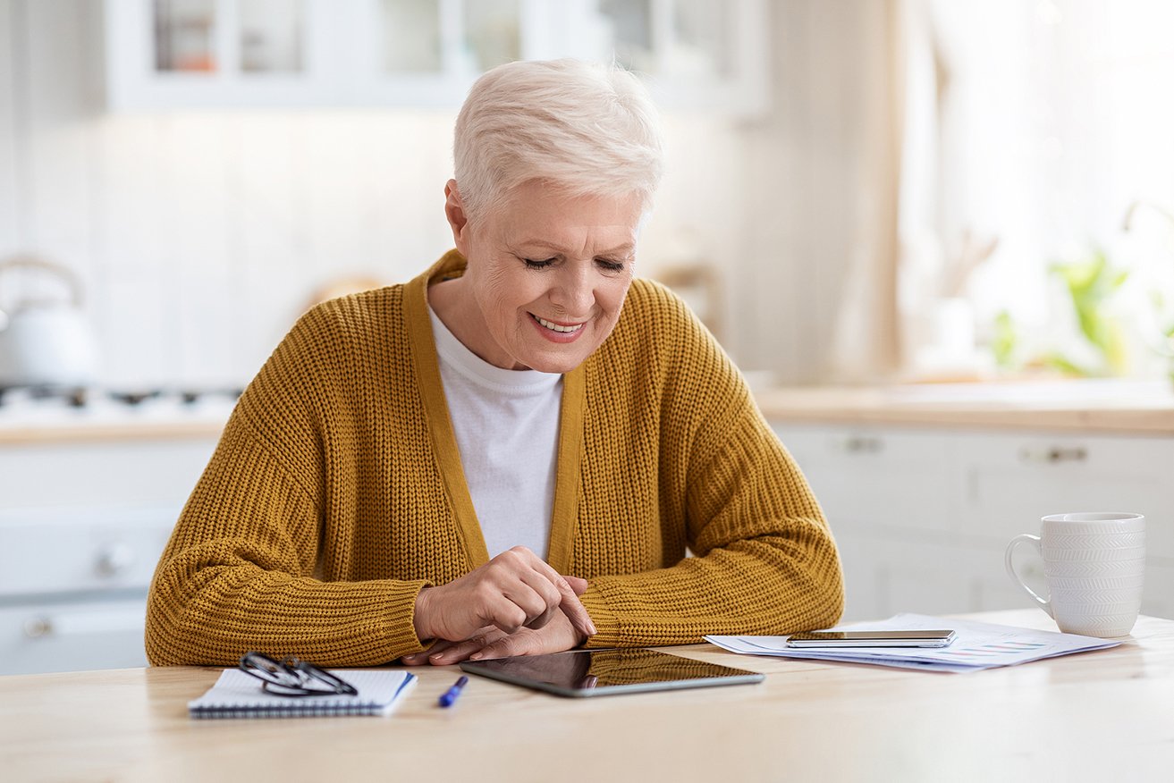 Senior woman at desk using tablet to research senior living options 