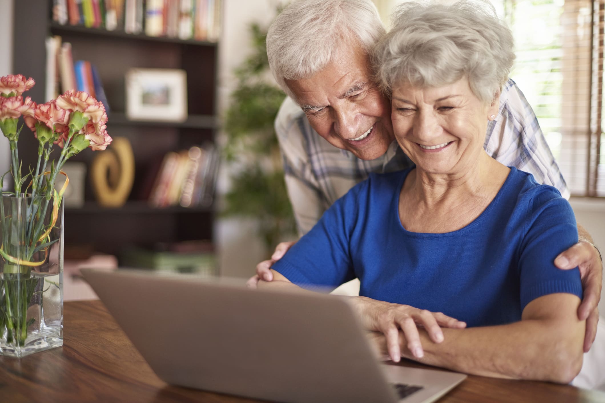 Senior couple smiling and looking at a laptop as they decide which type of senior living community is right for them