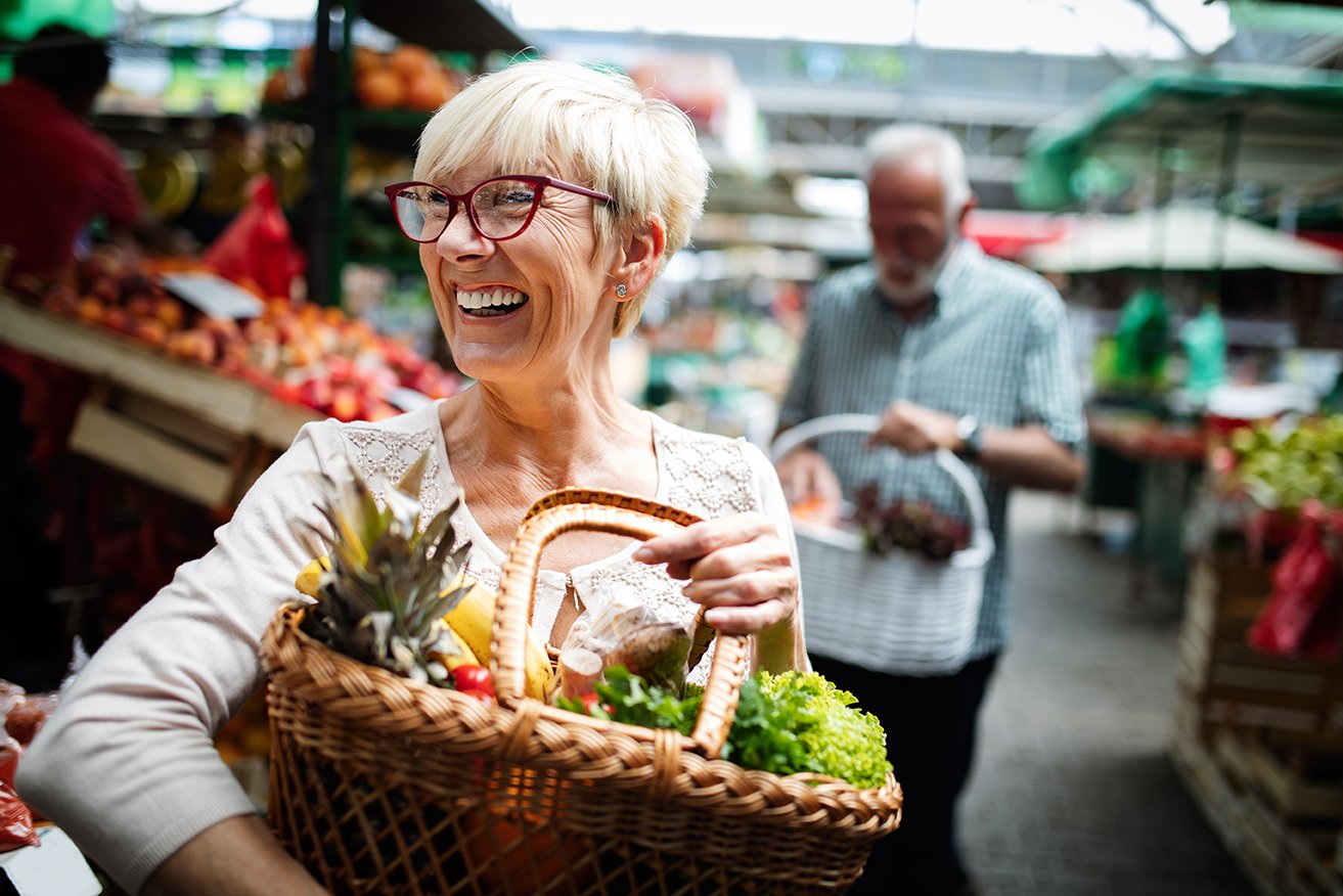 Senior woman in market with basket of fruit that contributes to healthy aging