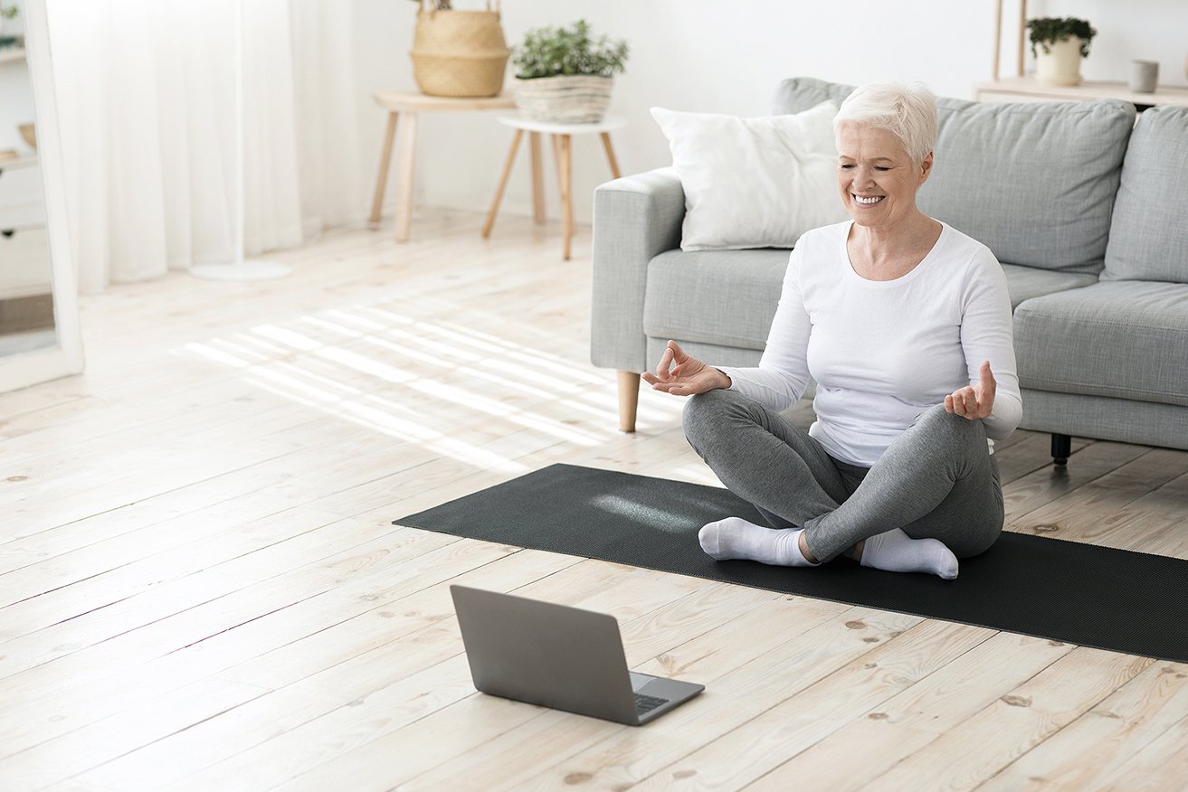 Senior woman in front of laptop doing virtual yoga and mindfulness exercises 
